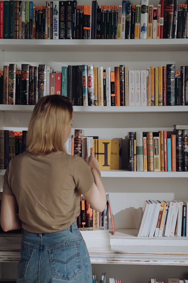 A young woman browses a library bookshelf, exploring various literature titles.