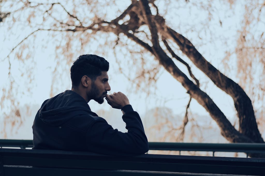 Man in deep thought sitting on a bench in a serene autumn park setting.