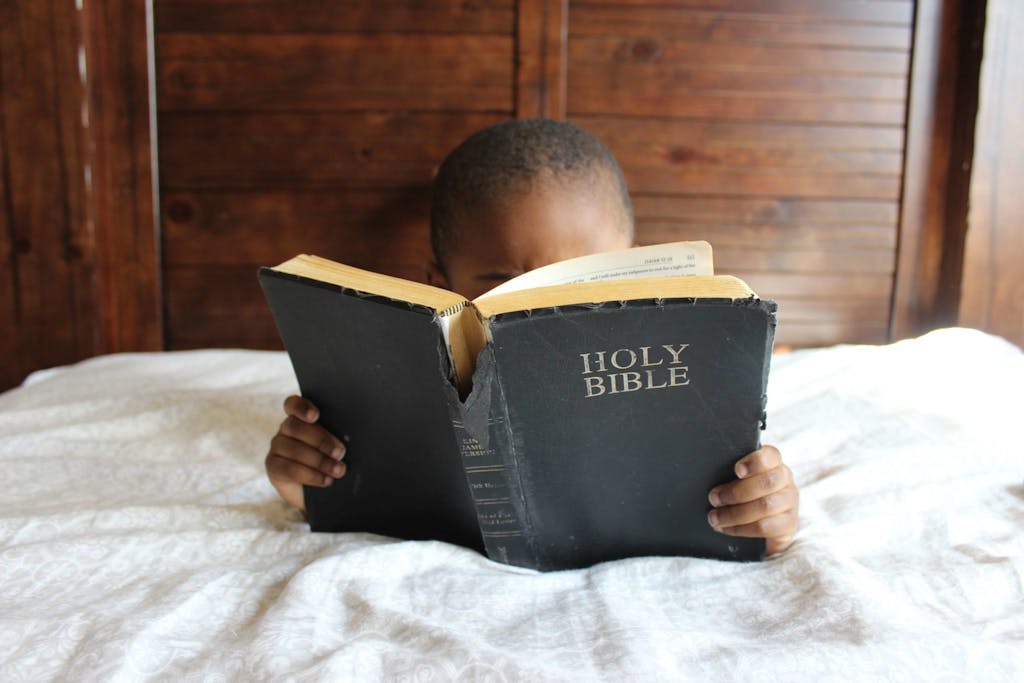 Young child reading a Holy Bible indoors, conveying a serene and religious atmosphere.