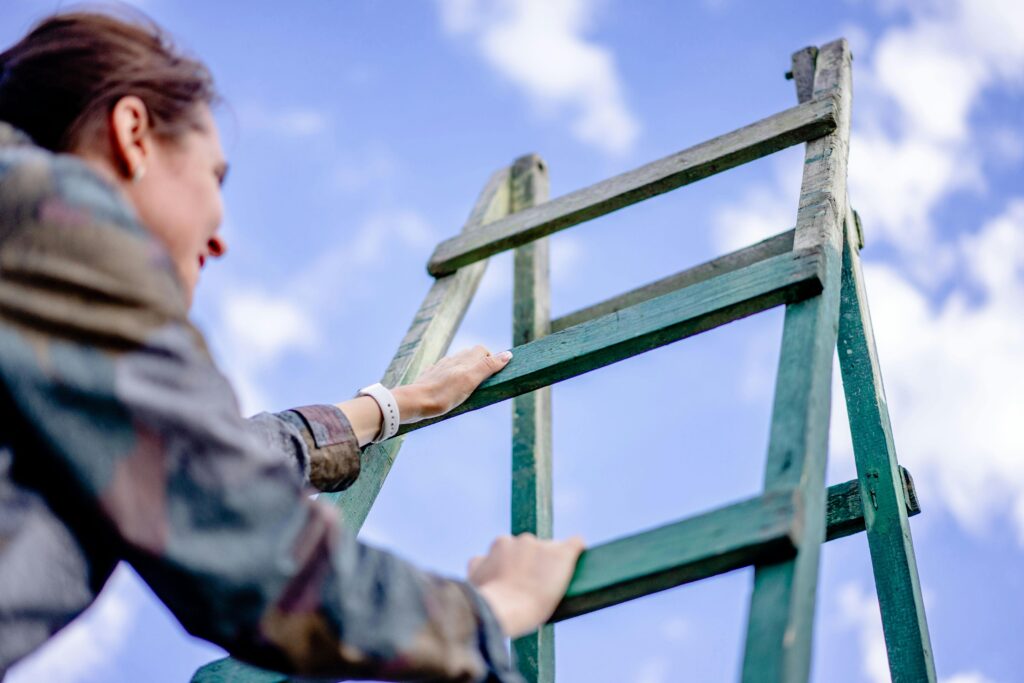 A woman climbs a green ladder under a bright blue sky. Outdoor shot.