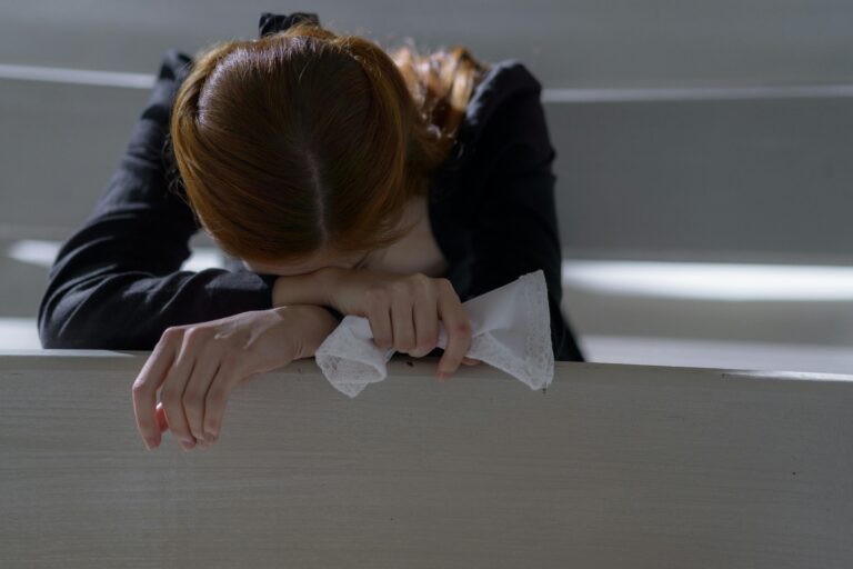 A woman leans on a bench in a peaceful church, lost in thought and prayer.